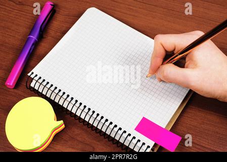 Man With Pen Writing Recent Updates On Notebook On Desk With Notes And Pencils. Businessman Presenting Important Message On Notepad On Table With Memos. Stock Photo
