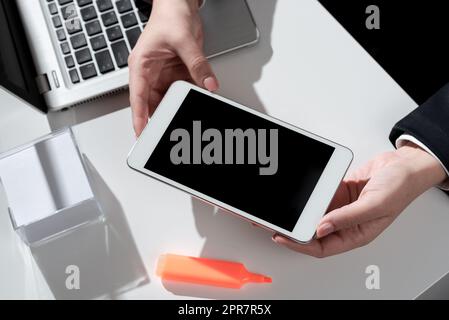 Businesswoman Presenting Important Message On Mobile Phone Screen On Desk With Notes, Marker And Lap Top. Woman Showing Crutial Information On Cellphone On Table With Computer Stock Photo