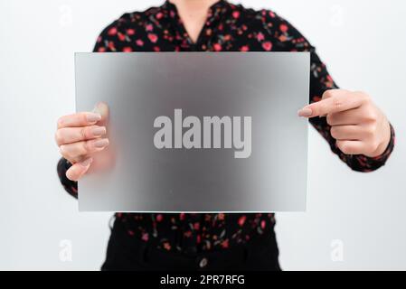 Businesswoman Holding And Pointing At Blank Placard While Making Important Announcement. Woman Wearing Floral T-Shirt Showing Board With New Ideas For Business Marketing. Stock Photo