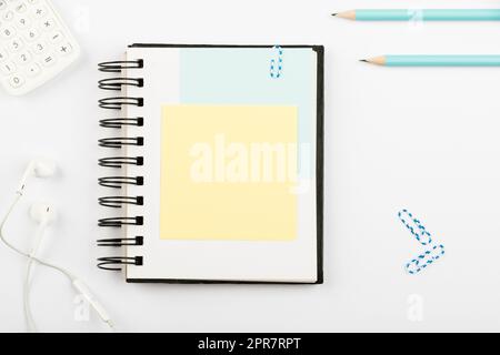 Notebook With Important Message On Desk With Pens, Calculator, Headphones And Paperclips. Notepad With Crutial Information On Table With Pencils And Colored Clips. Stock Photo