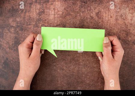 Hands Of Woman Holding Speech Bubble Of Pastel Color Paper Over Wooden Background. Businesswoman With Blank Sheet And Representing Thoughts And Opinions. Stock Photo