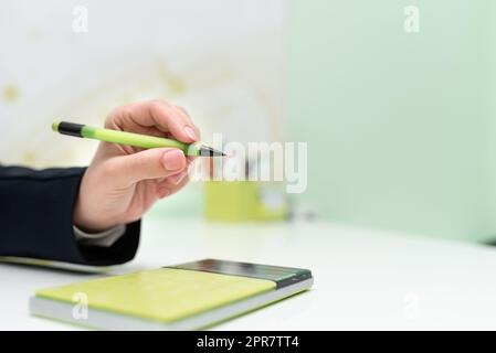 Businesswoman Pointing With Pen On Important Message With Calculator And Notebook On Desk. Woman Presenting News On Table With Notepad. Executive Displaying Recent News. Stock Photo