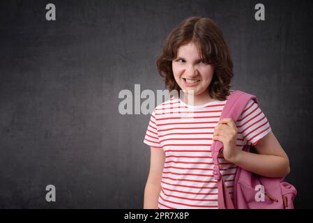 Angry schoolgirl holding backpack, looking at camera Stock Photo