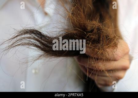 The girl holds the ends of damaged dry hair in her hand. Hair close-up. Stock Photo