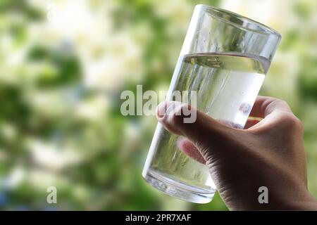 A glass of water in a hand close-up on a natural green background outdoors. Stock Photo
