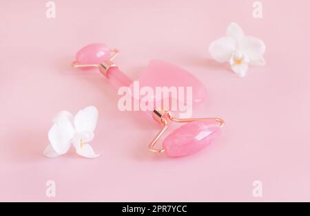 Facial roller and gua sha massager near white orchid flowers on light pink, close up Stock Photo