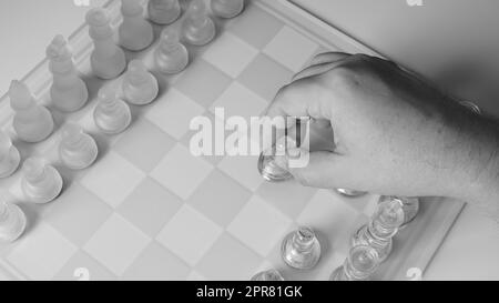 A chessboard with a hand starting to move a chess piece. Clear glass chess figures on a chessboard Stock Photo