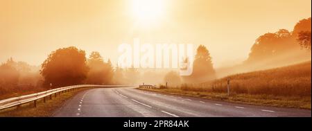 Black asphalt road with dividing line and safety fence in the morning mist. Stock Photo