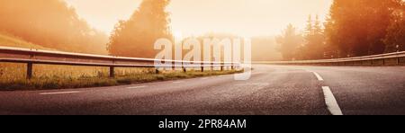 Black asphalt road with dividing line and safety fence in the morning mist. Stock Photo