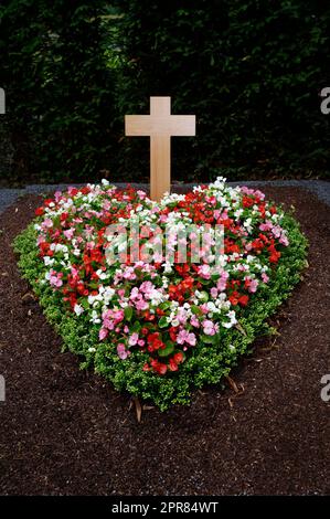 colorful heart shaped flower arrangement on a grave with wooden cross Stock Photo