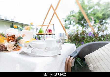Coffee cup and flowers bouquet on table in garden. Afternoon tea concept. Home outdoor furniture. Wicker chair and table with white tablecloth in vintage style. Cozy chair and table on the terrace. Stock Photo