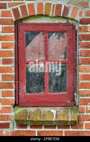 Closeup of abandoned red window covered in spiderwebs, algae and moss from neglect, poverty and economic crisis. Empty, old residential building or home in a village with damp mold on the windowsill Stock Photo