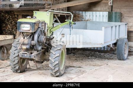 Typical heavy diesel walking tractor with trailer. Agricultural transport equipment of the countryside. Portable agricultural equipment, walking minitractor. The start system is mechanical and manual. Stock Photo