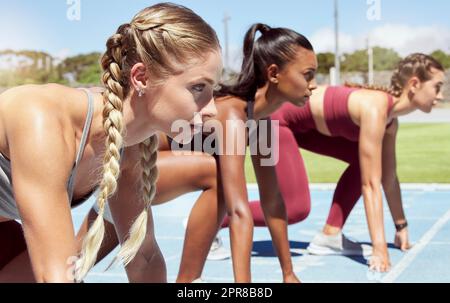 Three female athletes at the starting line in a track race competition at the stadium. Young sporty women in a race waiting and ready to run. Diverse sportswomen at the sprint line or starting blocks Stock Photo