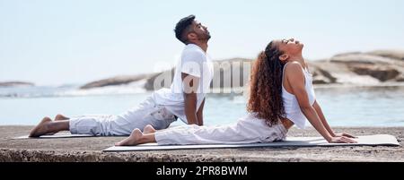 Good for the mind, body and soul. Full length shot of a young couple practicing yoga at the beach. Stock Photo