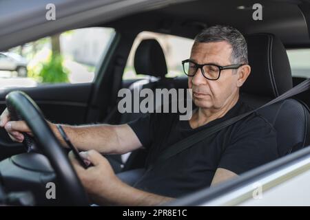 Senior in his 70s driving a car and using his mobile phone Stock Photo