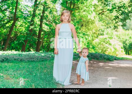 Two sisters in similar blue dresses are walking in the park Stock Photo