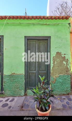 Old abandoned house or home with a weathered green wall and aging wooden door. Vintage and aged residential building built in a traditional architectural style or design with a cobble stone road Stock Photo