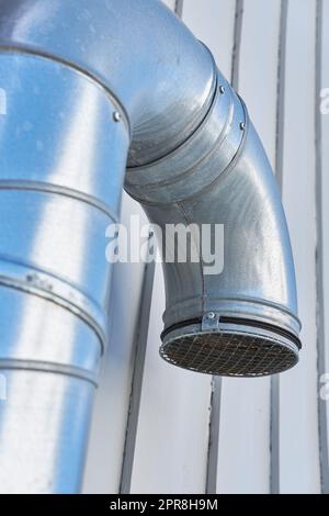 Closeup of a large metal ventilation pipe against the side of a building outside. Engineered stainless steel extractor fan system for fresh air. Galvanized structure for clean, healthy air and oxygen Stock Photo