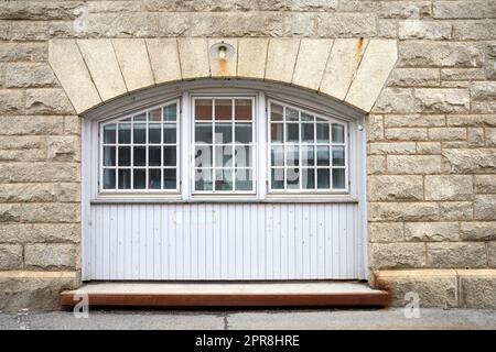 Oldwindow. Architecture of an old window in a brick wall. Facade of vintage white or classic windows on a house. Exterior details of a traditional, rustic residential building with light stone walls. Stock Photo