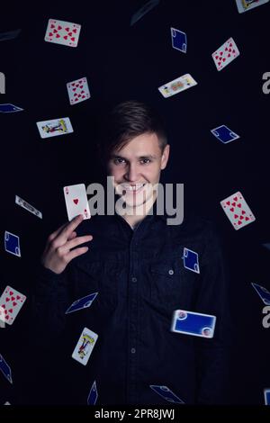 Successful young man holds up a victory lucky card. Gambler play luck games and win, isolated on dark background. Gambling jackpot winner with an ace of hearts under a rain of playing cards of hearts under a rain of playing cards Stock Photo