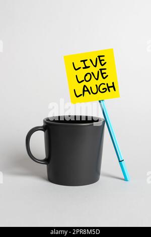 Writing displaying text Live Love Laugh. Business concept Be inspired positive enjoy your days laughing good humor Cup, Pen And Sticky Note With Important Announcement On Desk. Stock Photo