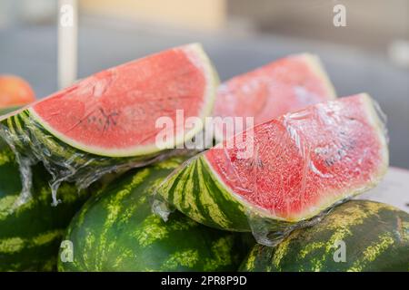 Watermelons in the market. Fresh watermelons are stacked on the counter, cut into pieces and wrapped in plastic wrap to keep fresh. Stock Photo