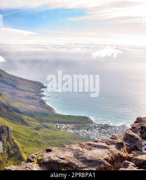 Landscape of Lions Head mountain with houses, ocean and cloudy sky with copy space. Perspective view of green mountains with lots of vegetation overlooking an urban city in Cape Town, South Africa Stock Photo