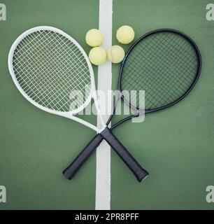 Above view of two tennis rackets and balls on an empty court in a sports club. Aerial view of black and white tennis gear and equipment on asphalt. Ready to play a competitive game versus an opponent Stock Photo