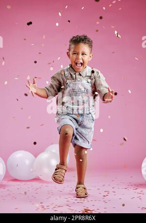 A cute little mixed race boy celebrating and winning against a pink copyspace background in a studio. African child looking excited at a gender reveal party with confetti and balloons Stock Photo