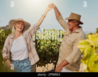 Smiling senior couple dancing together and feeling playful on vineyard. Caucasian husband and wife standing together and enjoying a day on a farm after wine tasting weekend. Man and woman having fun Stock Photo