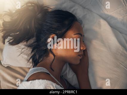 A beautiful young mixed race woman sleeping in a soft comfortable bed at home. One hispanic female feeling exhausted and resting in a comforting bed Stock Photo