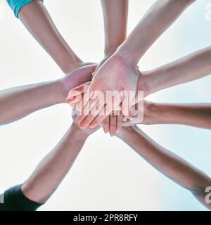 Closeup of diverse group of people from below stacking hands together in a pile to express unity, support and trust. Multiracial community huddled in a circle to celebrate winning achievement. Joining for collaboration and team spirit Stock Photo