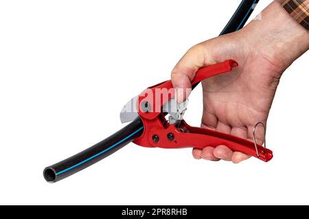 Plumber tools isolated. A man accurately cuts a piece of PE pressure pipe or water pipe with a red pvc pipe cutter. Clipping path. Drinking and service water systems. Stock Photo