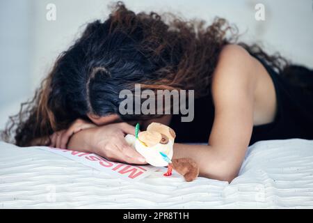 I just wish I knew where they were.... a young woman looking sad while holding a teddy bear and lying on a bed alongside a missing person poster. Stock Photo