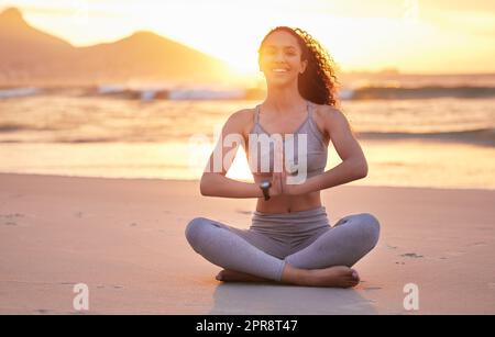 Happy from the inside, out. a young woman practicing yoga on the beach. Stock Photo