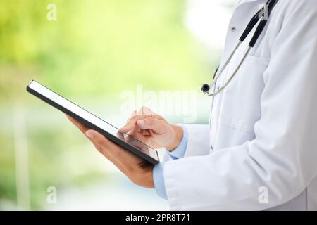 Closeup of female doctor working on her digital tablet in the office. A unknown mixed race and professional young woman working in a hospital office. Health resources are easy to find online Stock Photo