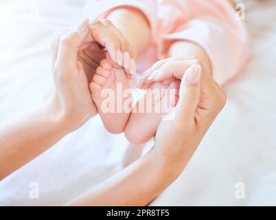 Mother holding baby feet. Closeup of tiny newborn baby feet held by a parent. Small baby toes. Little baby lying on a bed. Woman holding feet of little baby girl. Innocent infant being held by mother Stock Photo