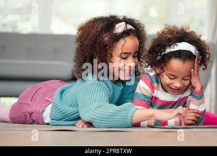 Taking turns to enjoy their favourite digital games. two little girls playing on a digital tablet together at home. Stock Photo