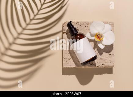 One pump bottle on stone near white orchid flowers on light yellow top view, Cosmetic Mockup Stock Photo