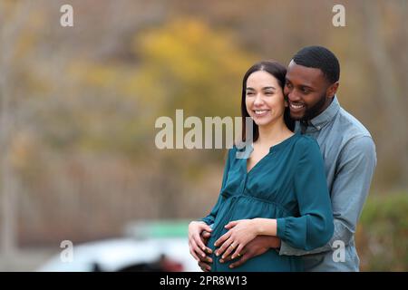 Interracial couple looking away enjoying pregnancy Stock Photo