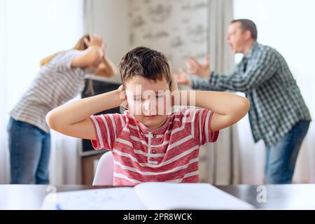 Sad child covers his ears with his hands during an argument between his parents Stock Photo