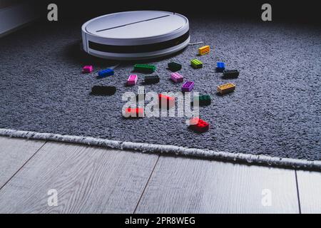 A robot vacuum cleaner cleans children's toys on the floor. Carpet and laminate cleaning. Assembling cubes with a robot vacuum cleaner.. Stock Photo