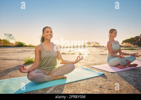 Full length yoga women meditating with legs crossed for outdoor practice in remote nature. Mixed race and caucasian mindful active people bonding and balancing for mental health. Young, serene and zen Stock Photo