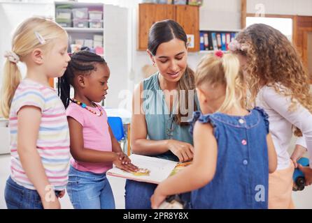 A preschool is the beginning of the learning experience. a young woman reading to her preschool students. Stock Photo