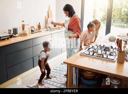 A happy mixed race family of five cooking and having fun in a kitchen together. Loving black single parent bonding with her kids while teaching them domestic skills at home Stock Photo