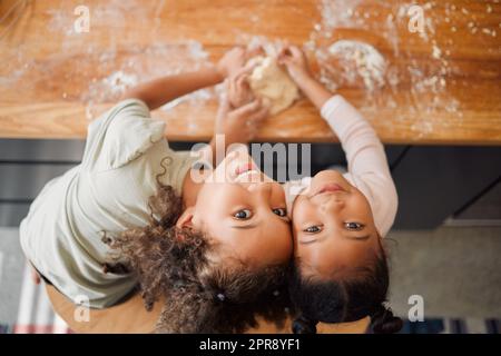 Two happy mixed race sisters having fun while baking together at home. Children only being playful while learning to cook in a kitchen Stock Photo