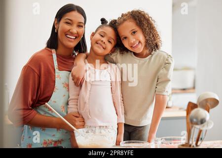 Females only, happy mixed race family of three cooking in a messy kitchen together. Loving black single parent bonding with her daughters while teaching them domestic skills at home Stock Photo