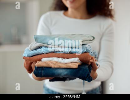 Woman cleaning a pile of laundry. Woman holding a stack of neat, folded clothing. Hands of a woman doing housework chores. Hispanic woman holding fresh, washed clothing and bedding. Stock Photo