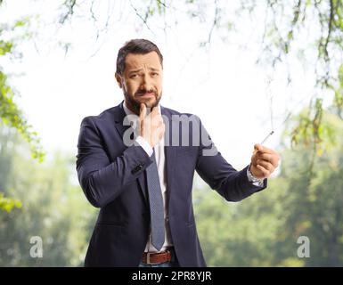 Doubtful young man holding a cigarette in a park and looking at camera Stock Photo